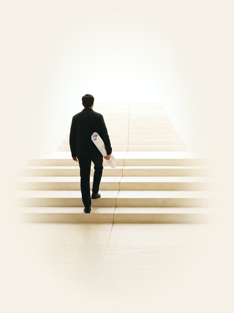 A person climbing broad ivory steps carrying a rolled plan